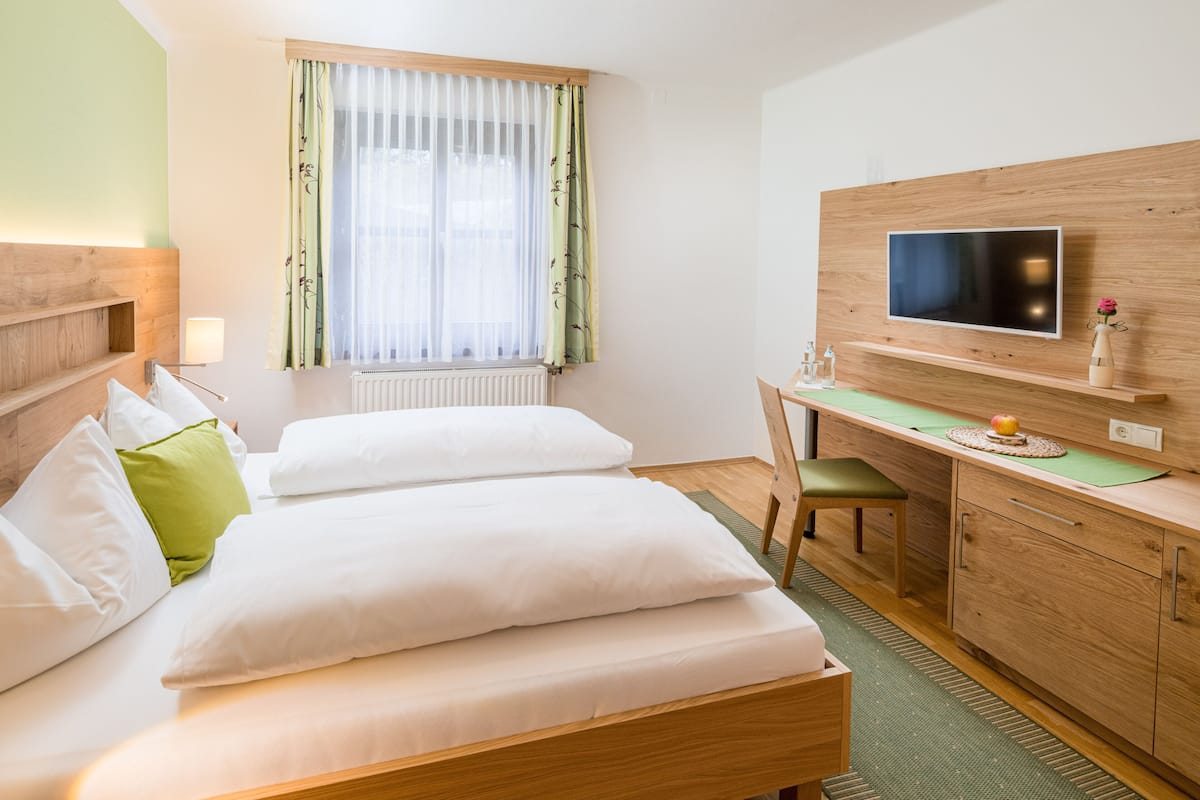 Ein Hotelzimmer mit zwei Betten, einem Schreibtisch, einem Fernseher und einem Fenster mit Vorhängen.