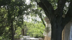A patio with a round table and chairs, surrounded by trees and a building. - rental in the heart of Provence with private pool secured (Grans)