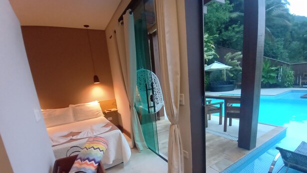 A bedroom with a bed, bedside table, and a view of an outdoor swimming pool. - Pousada Recanto El Shadday (Ubatuba)