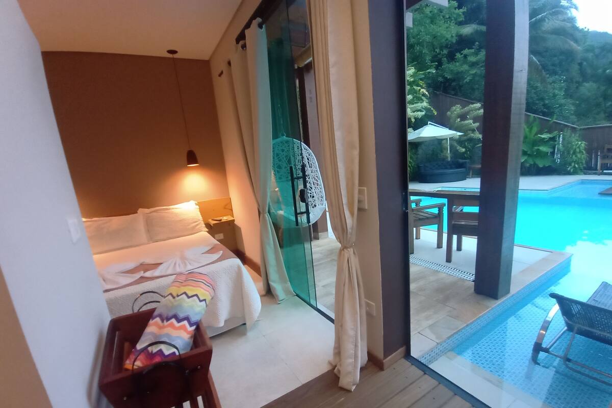 A bedroom with a bed, bedside table, and a view of an outdoor swimming pool.