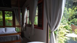 A bedroom with a large window, a bed with white bedding, and a bathtub. - Pousada Recanto El Shadday (Ubatuba)