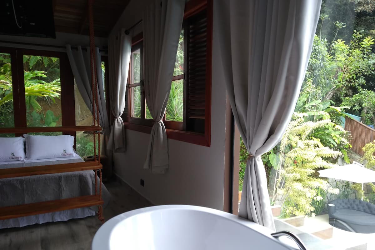 A bedroom with a large window, a bed with white bedding, and a bathtub.