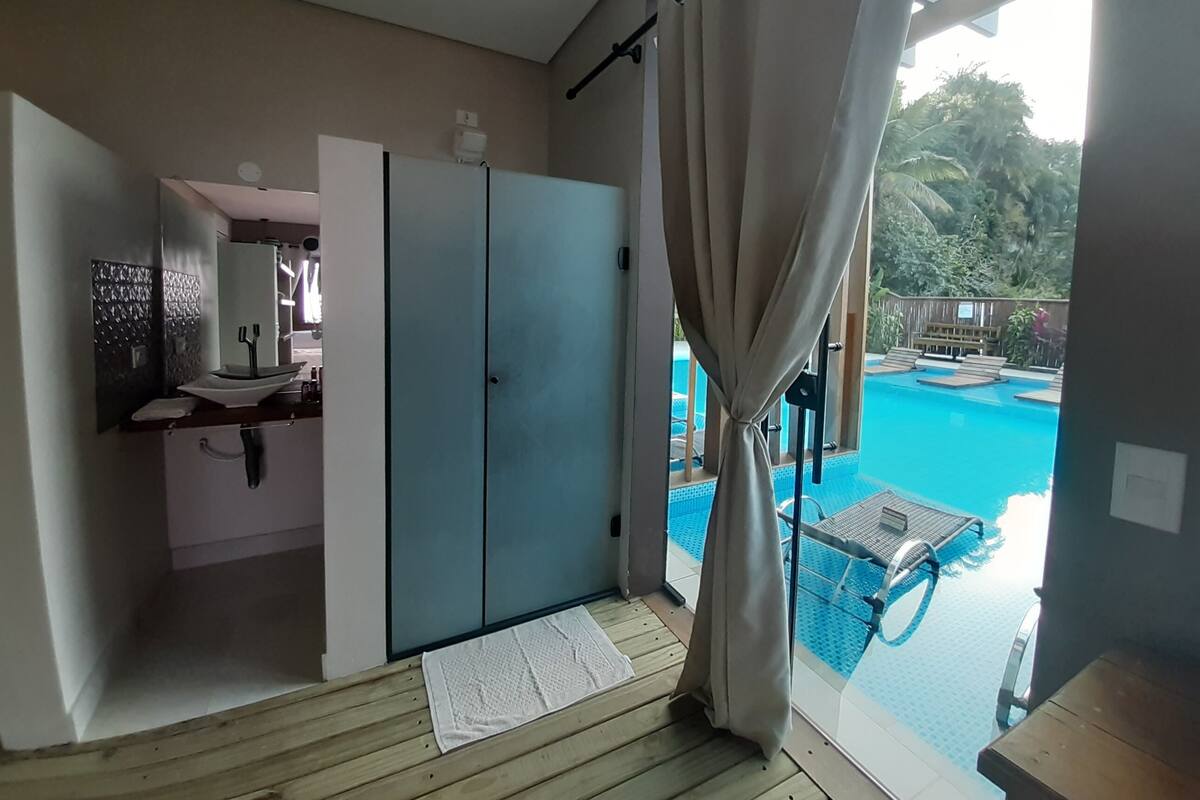 A room with a wooden floor, a sink, a mirror, a wardrobe, and a view of an outdoor swimming pool.