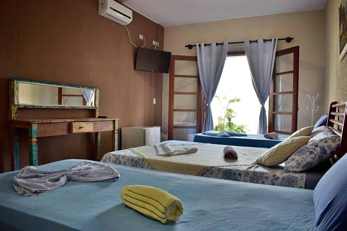 A hotel room with two beds, a TV, a desk, and a window with curtains.