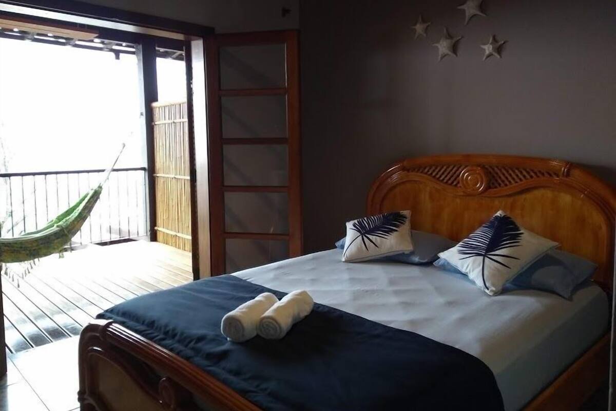 A bedroom with a bed, pillows, and a hammock outside the window.