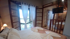 A hotel room with a bed, a TV mounted on the wall, and a balcony with a hammock. - Pousada Recanto El Shadday (Ubatuba)