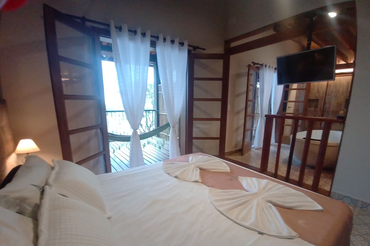 A hotel room with a bed, a TV mounted on the wall, and a balcony with a hammock.