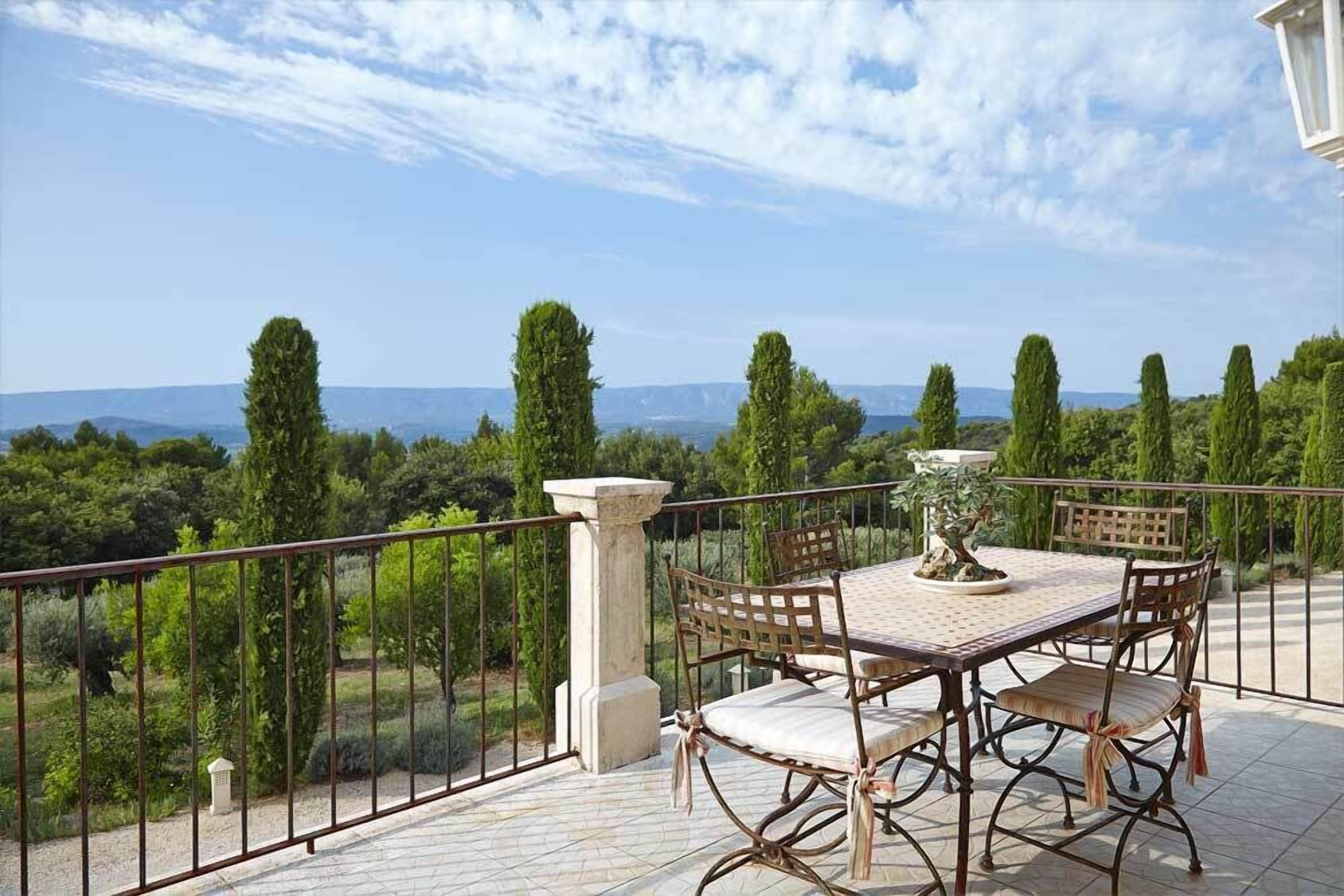Una terraza con mesa y sillas, con vistas a un paisaje pintoresco con árboles y colinas a lo lejos.