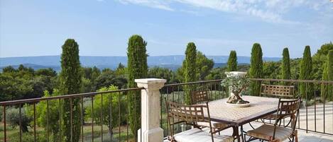 Una terraza con mesa y sillas, con vistas a un paisaje pintoresco con árboles y colinas a lo lejos.