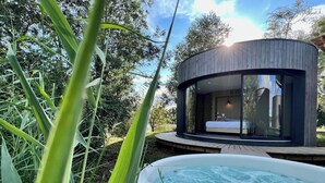 Una estructura circular moderna de madera con fachada de vidrio, junto a un jacuzzi en un exuberante jardín.
