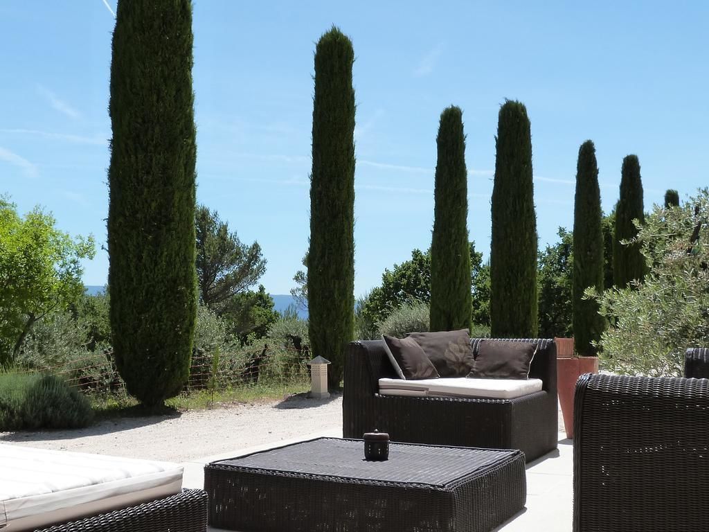 Un'area patio con un divano, un tavolino da caffè e alti cipressi sullo sfondo.