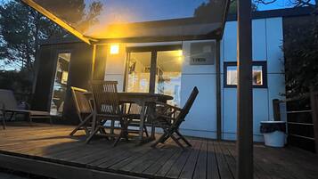 Un área de comedor exterior moderna con una mesa y sillas de madera, un espacio de estar techado y un edificio con un cartel que dice "TAOS".
