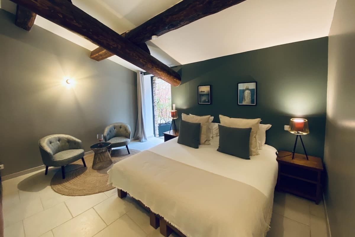 Une chambre à coucher avec un grand lit, deux fauteuils, une petite table et une table de chevet avec une lampe.