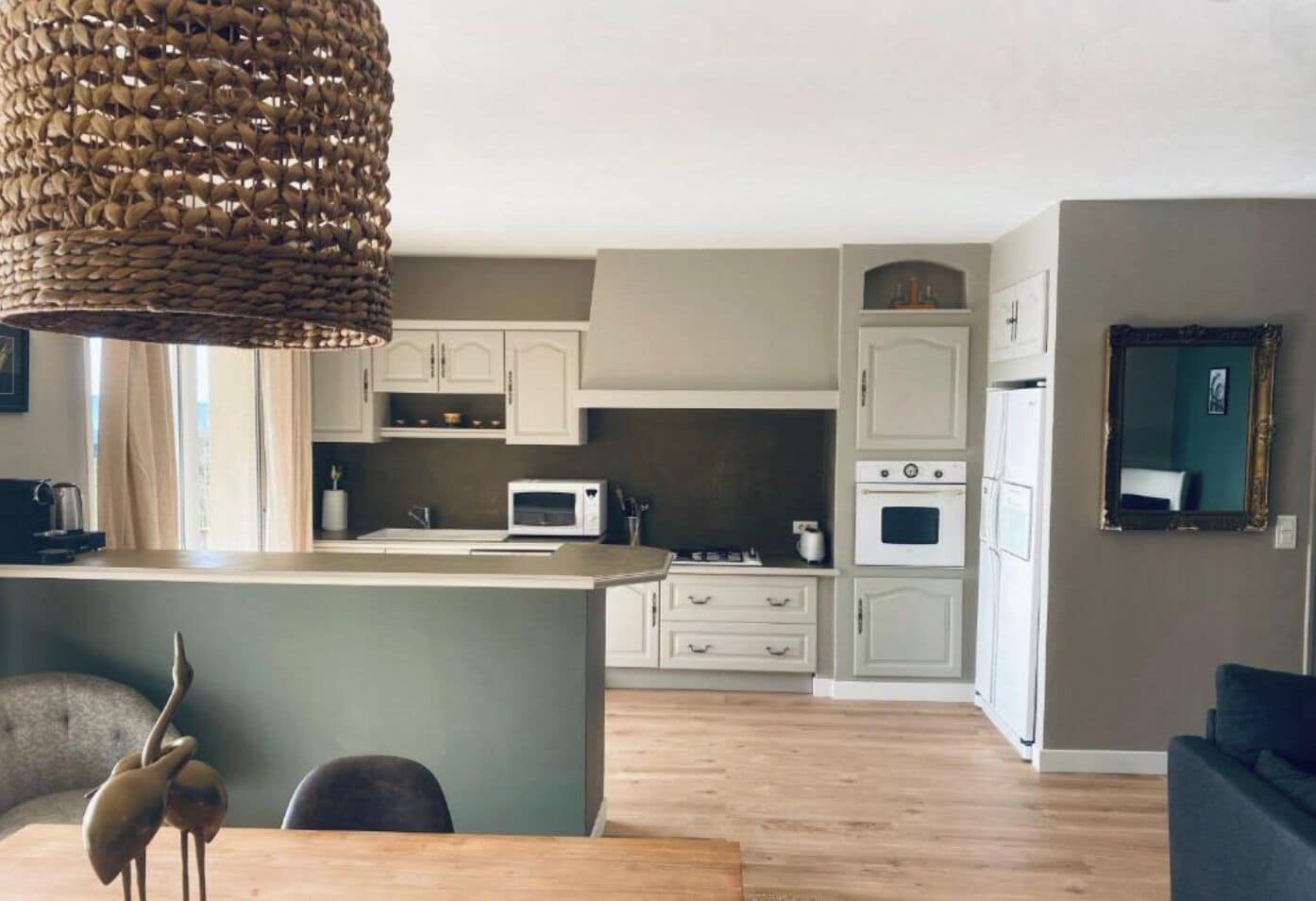 A modern kitchen with white cabinets, a microwave, and a stove. There is a dining area with a table and chairs, and a large woven light fixture above the island.