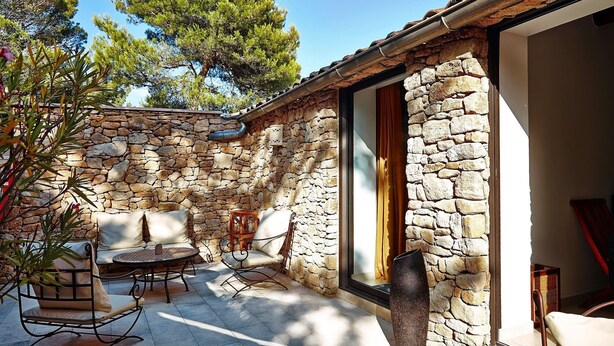 Une terrasse extérieure entourée de murs en pierre, avec une table ronde et deux chaises, un mur en pierre et une vue sur les arbres.