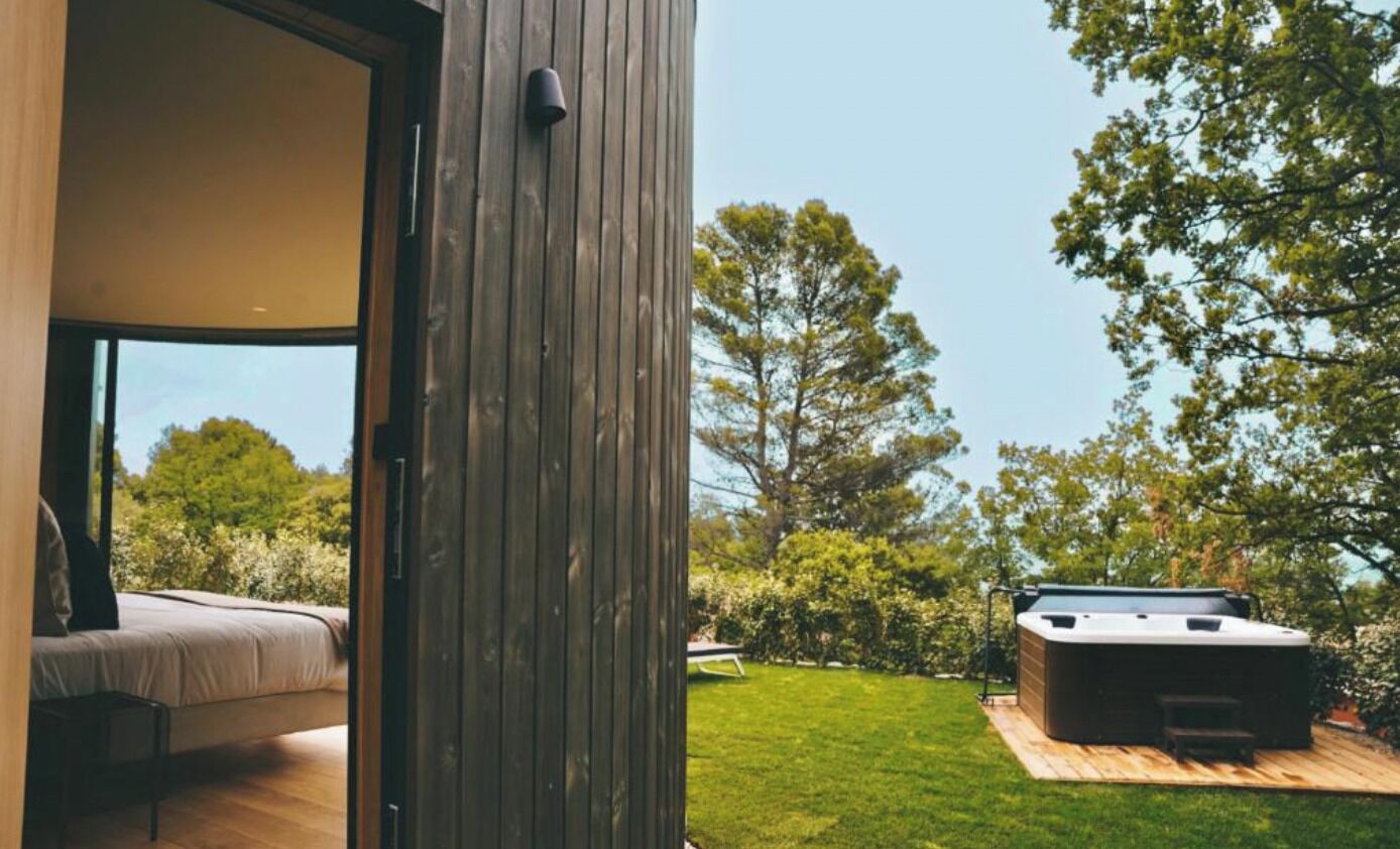 Un área moderna de hidromasaje al aire libre con una terraza de madera, rodeada de abundante vegetación y árboles.