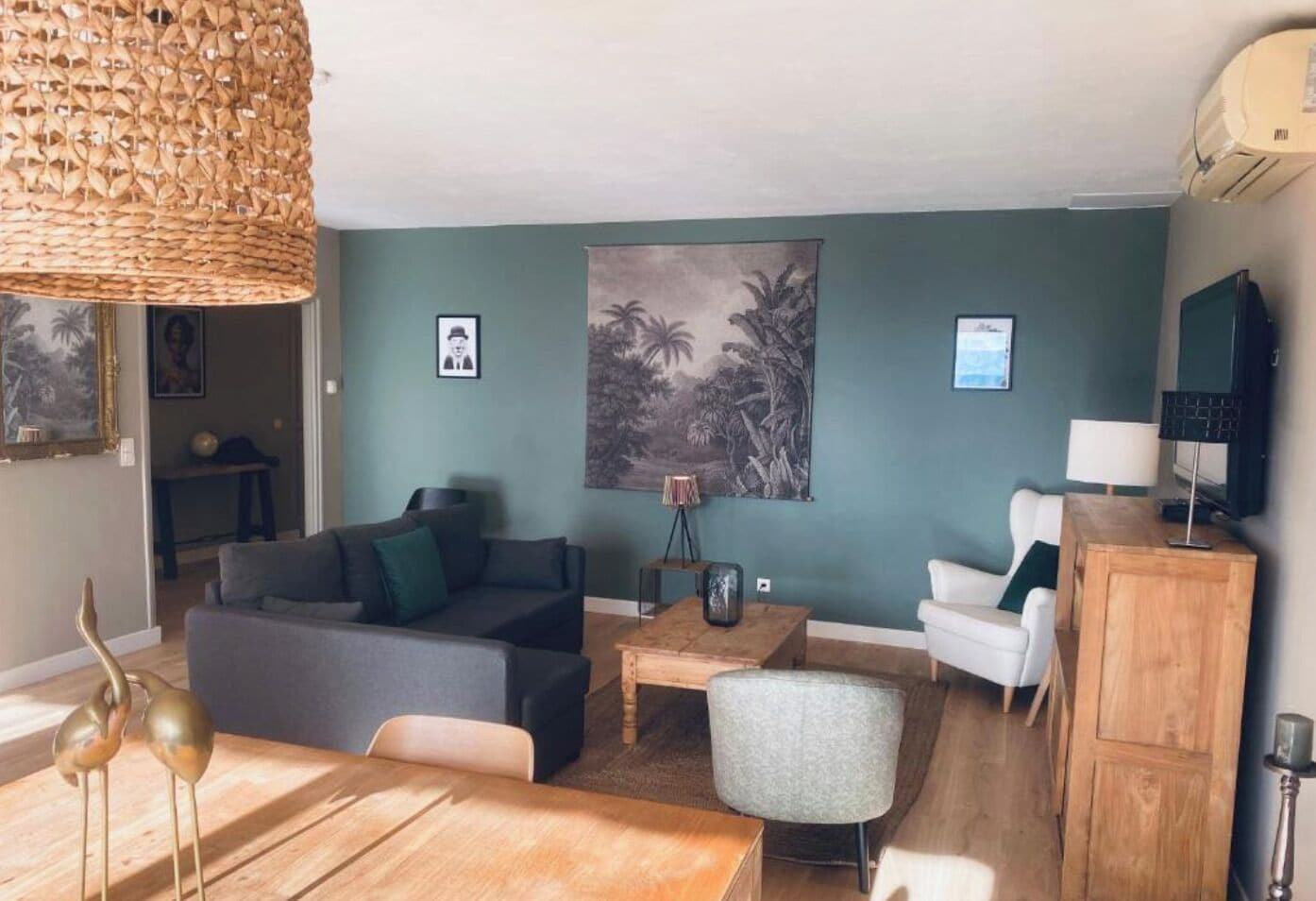 A living room with a sofa, chairs, a coffee table, and a dining table. There is a painting on the wall and a lamp on a side table.