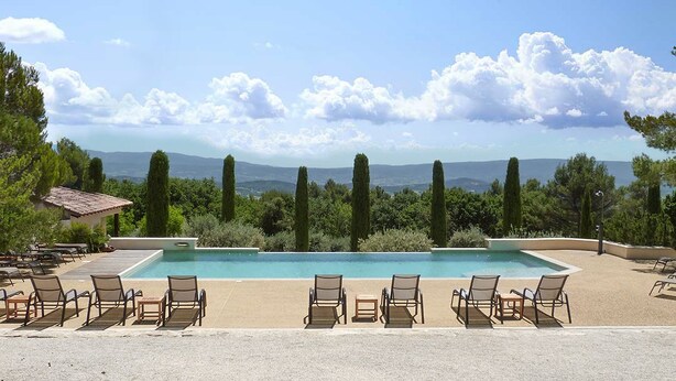 Un área de piscina con sillas de descanso, una mesita y vistas al paisaje.