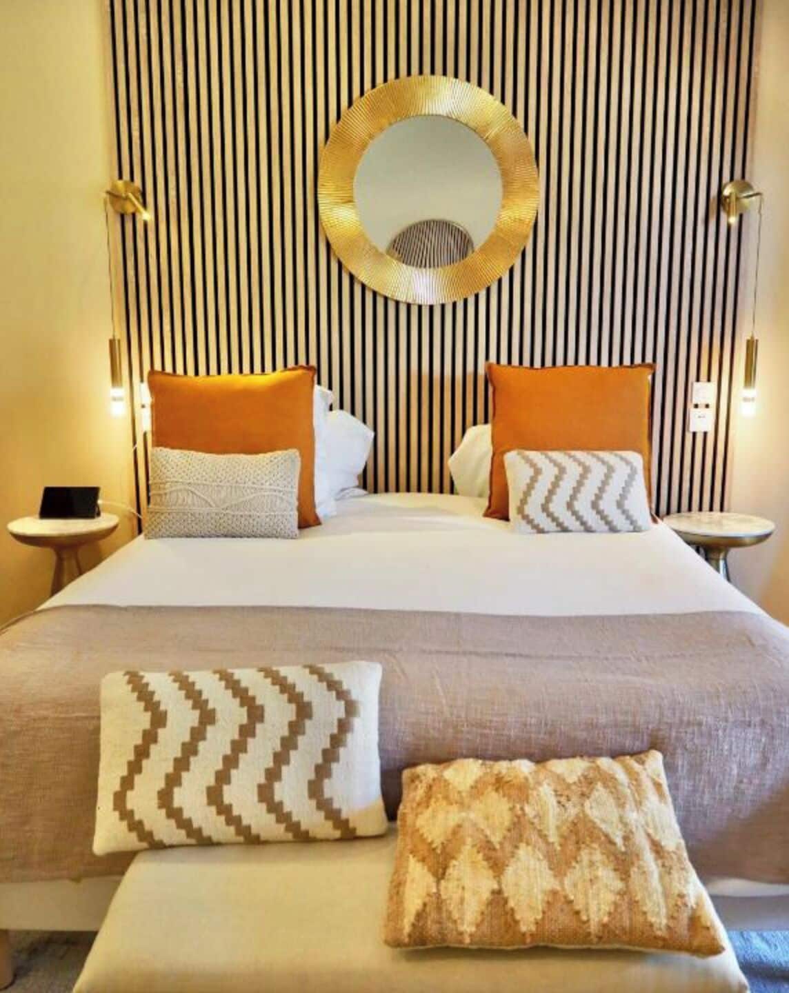 A hotel room with a large bed, striped wallpaper, a round mirror, and multiple pillows.