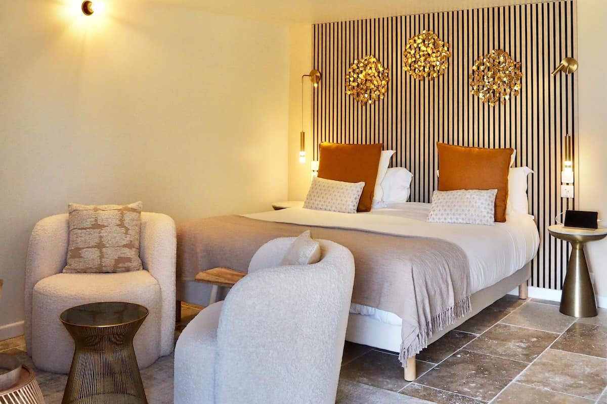 Une chambre à coucher comprenant un lit, deux fauteuils, une petite table d’appoint, un panneau décoratif mural et un balcon avec une balustrade.