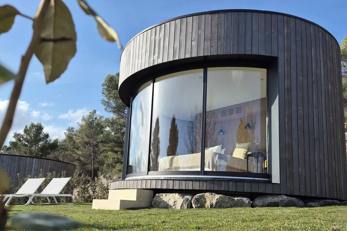 Un bâtiment moderne de forme circulaire, doté de grandes fenêtres, d’un toit plat et d’une pelouse verdoyante agrémentée de chaises longues.
