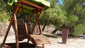 A wooden swing chair with a green canopy, set against a backdrop of trees and a stone wall.