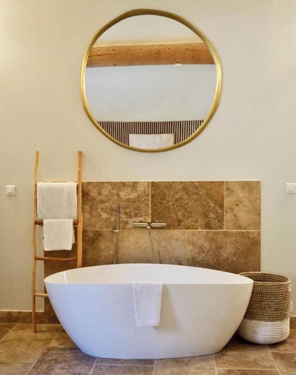 Une salle de bain moderne avec une baignoire sur pieds, une échelle en bois, un miroir rond et un mur recouvert de carreaux.
