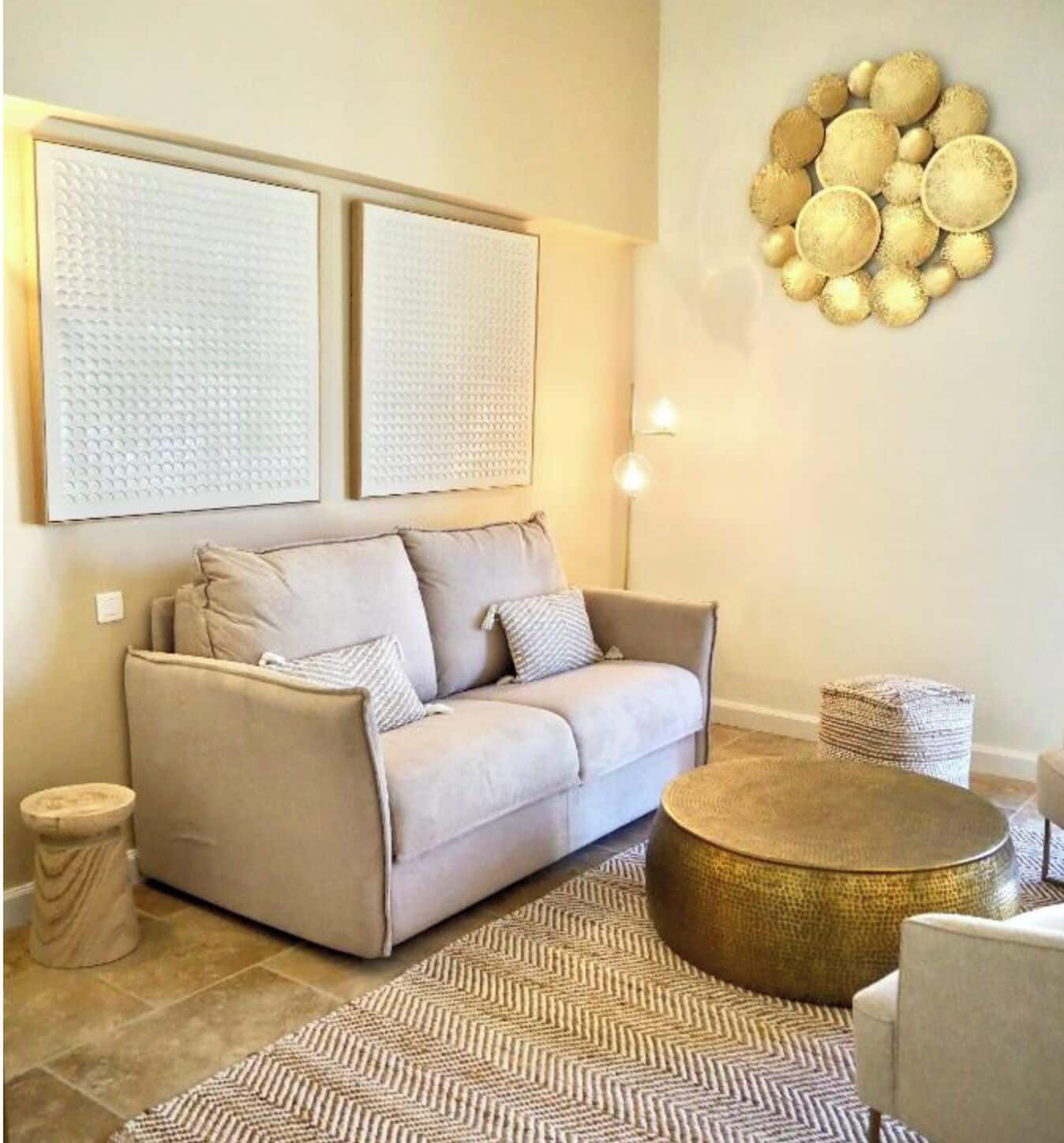 A living room with a beige sofa, a round coffee table, a patterned rug, and wall art.