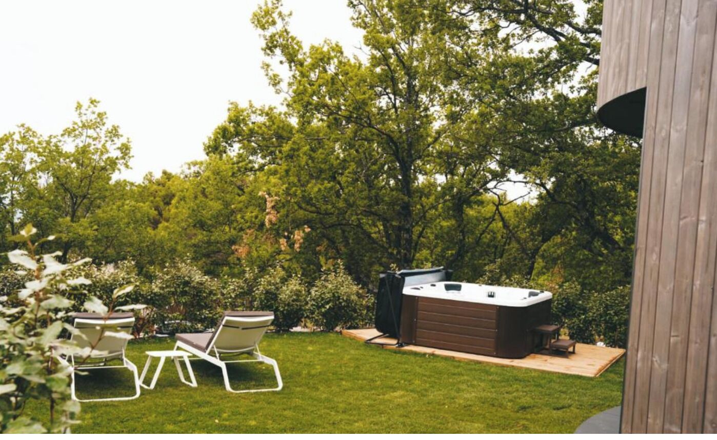 A backyard with a hot tub, two lounge chairs, and a wooden deck.