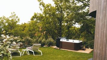A backyard with a hot tub, two lounge chairs, and a wooden deck.