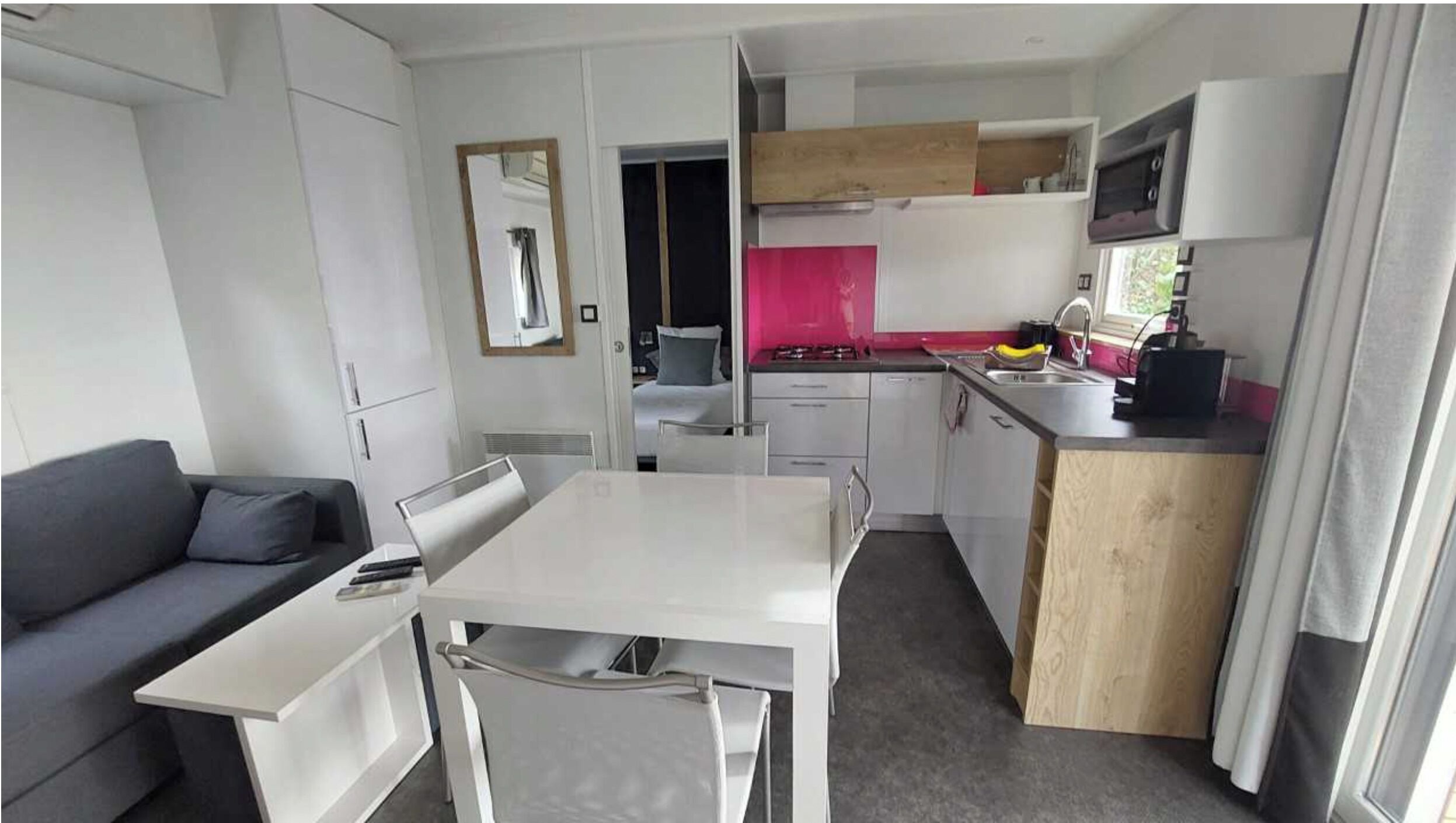 Una kitchenette compacta con estufa, pileta y microondas. Hay un pequeño comedor con una mesa y sillas. Un sofá gris se encuentra en la zona de estar.