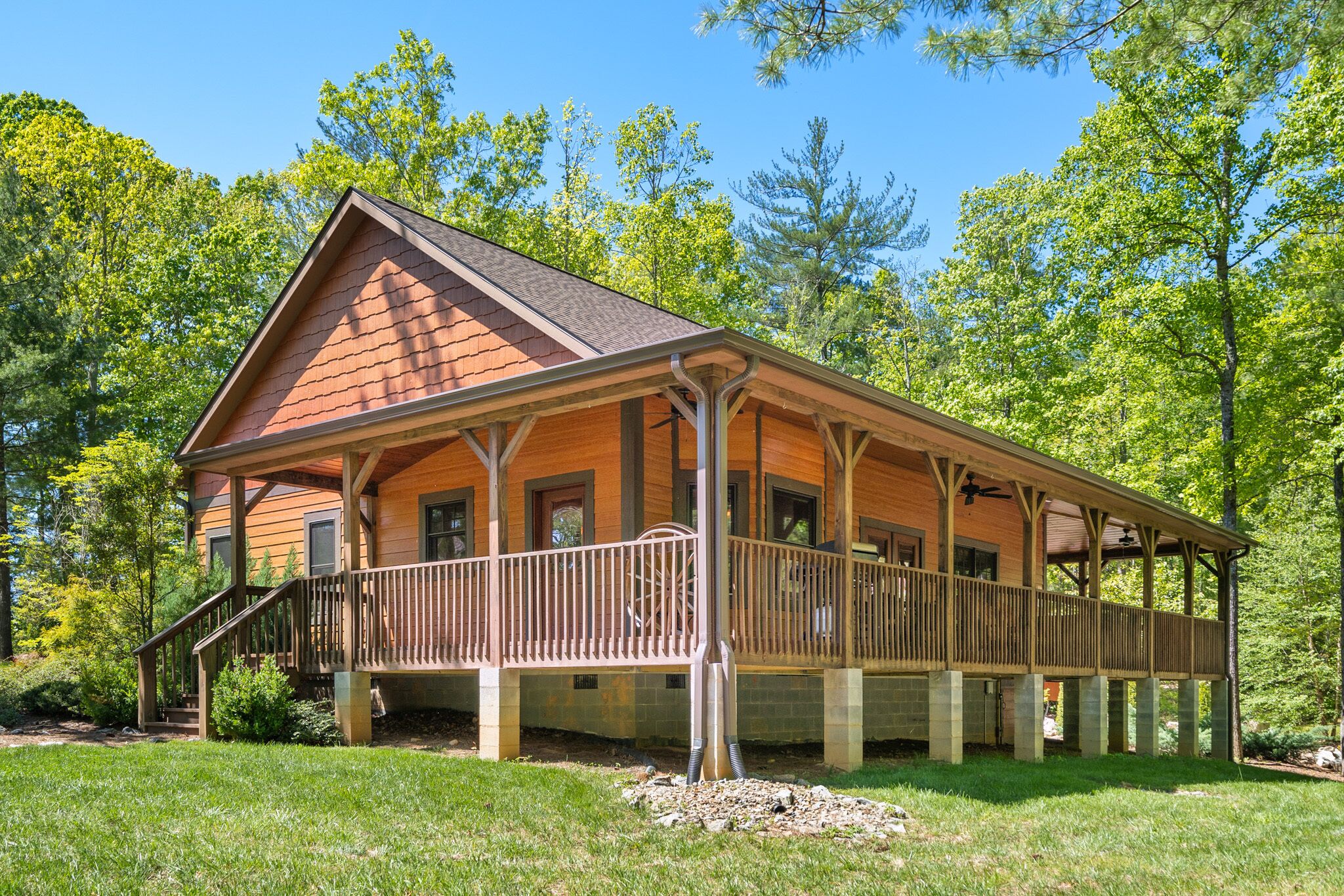 A wooden cabin with a porch, surrounded by trees.
