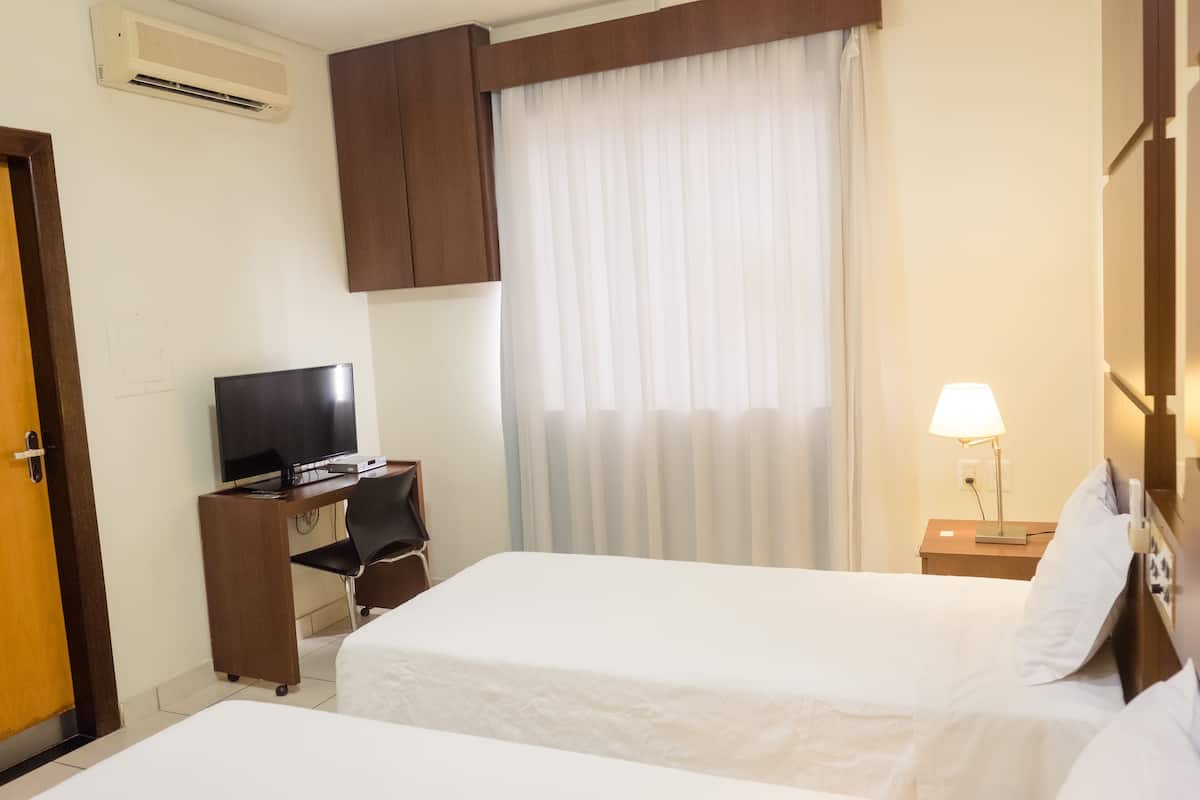 A hotel room with two beds, a desk with a TV, a lamp, and an air conditioner.