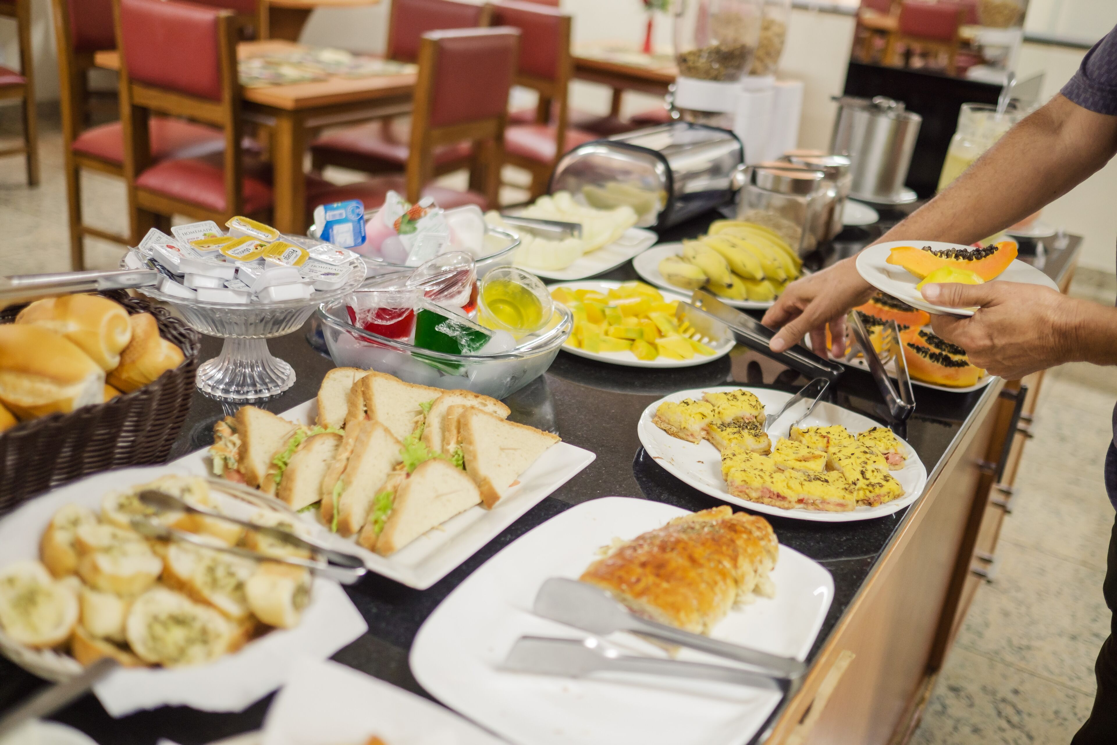 A buffet with various food items including sandwiches, fruits, and a slice of cake.