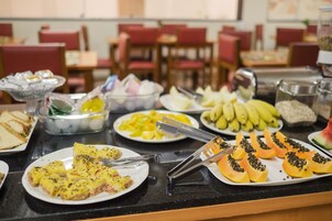 Una mesa de buffet con diversos alimentos, como sándwiches, fruta y un plato con cobertura verde.