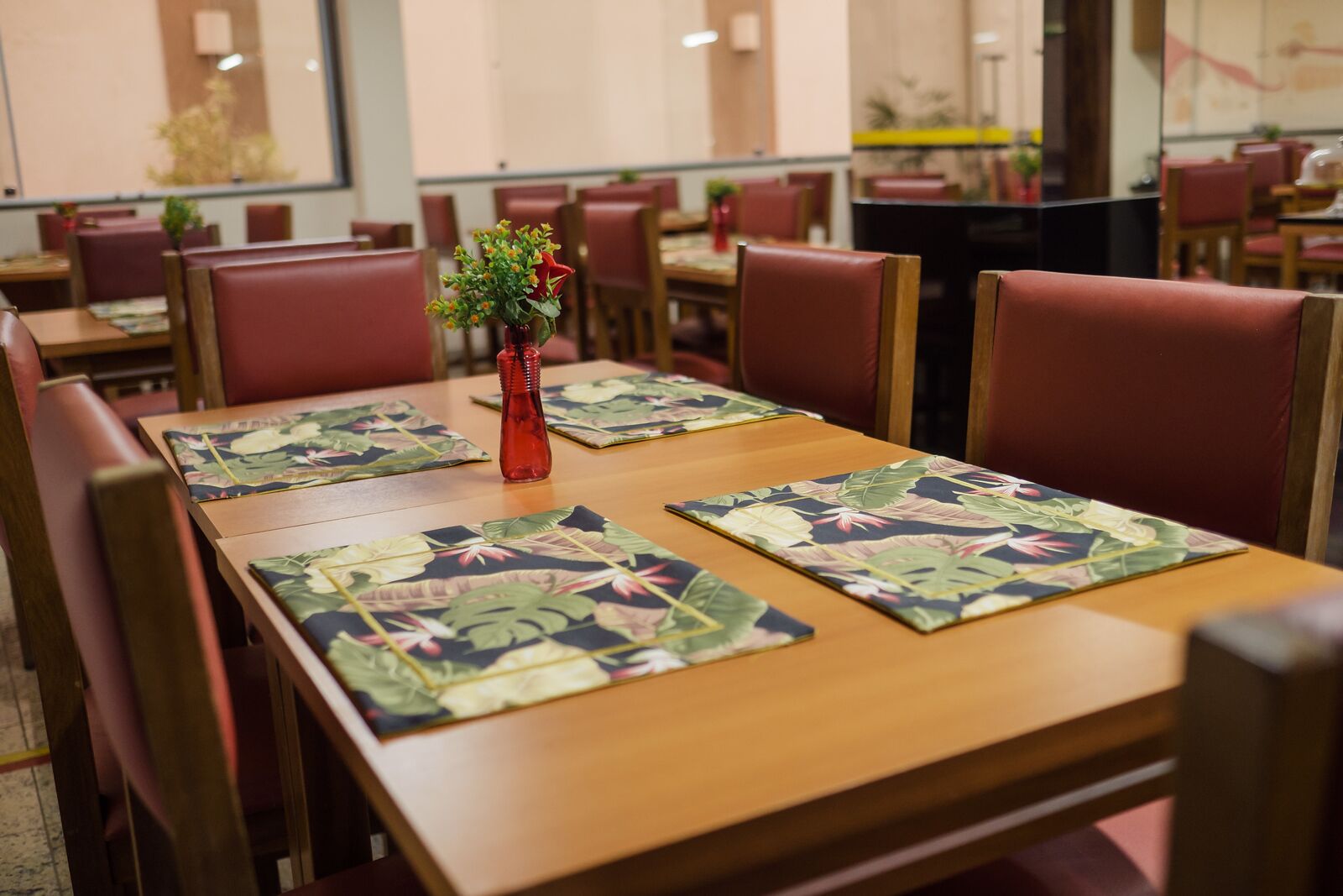A dining area with wooden tables, red cushioned chairs, and floral placemats.