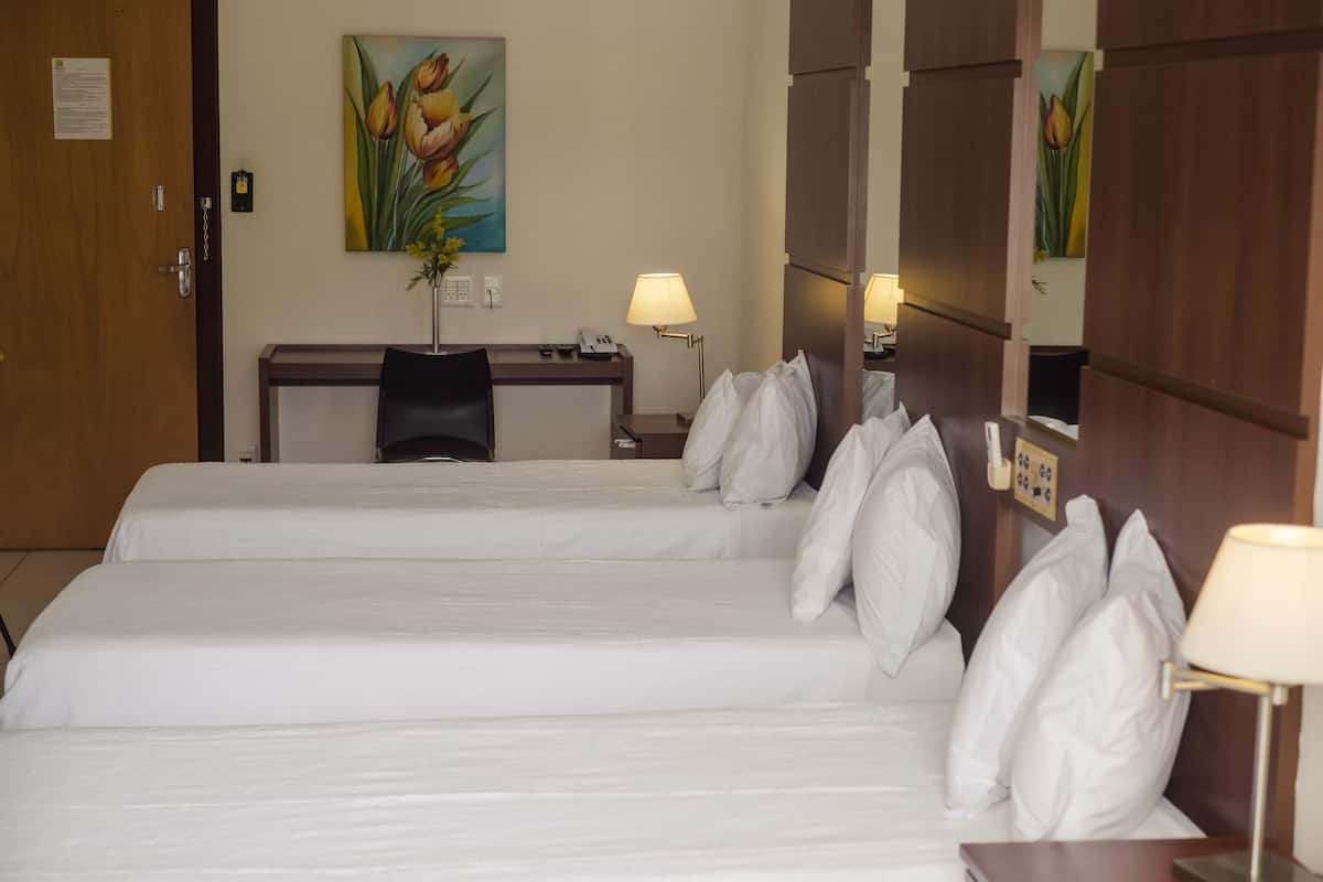 A hotel room with two beds, a desk, a chair, and a lamp.
