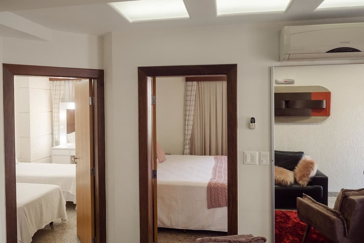 A hotel room with two beds, a sitting area with a sofa and armchair, and a ceiling fan.
