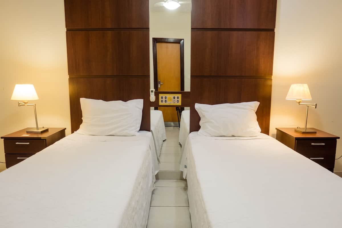 A hotel room with two beds, a wooden headboard, a mirror, and bedside lamps.