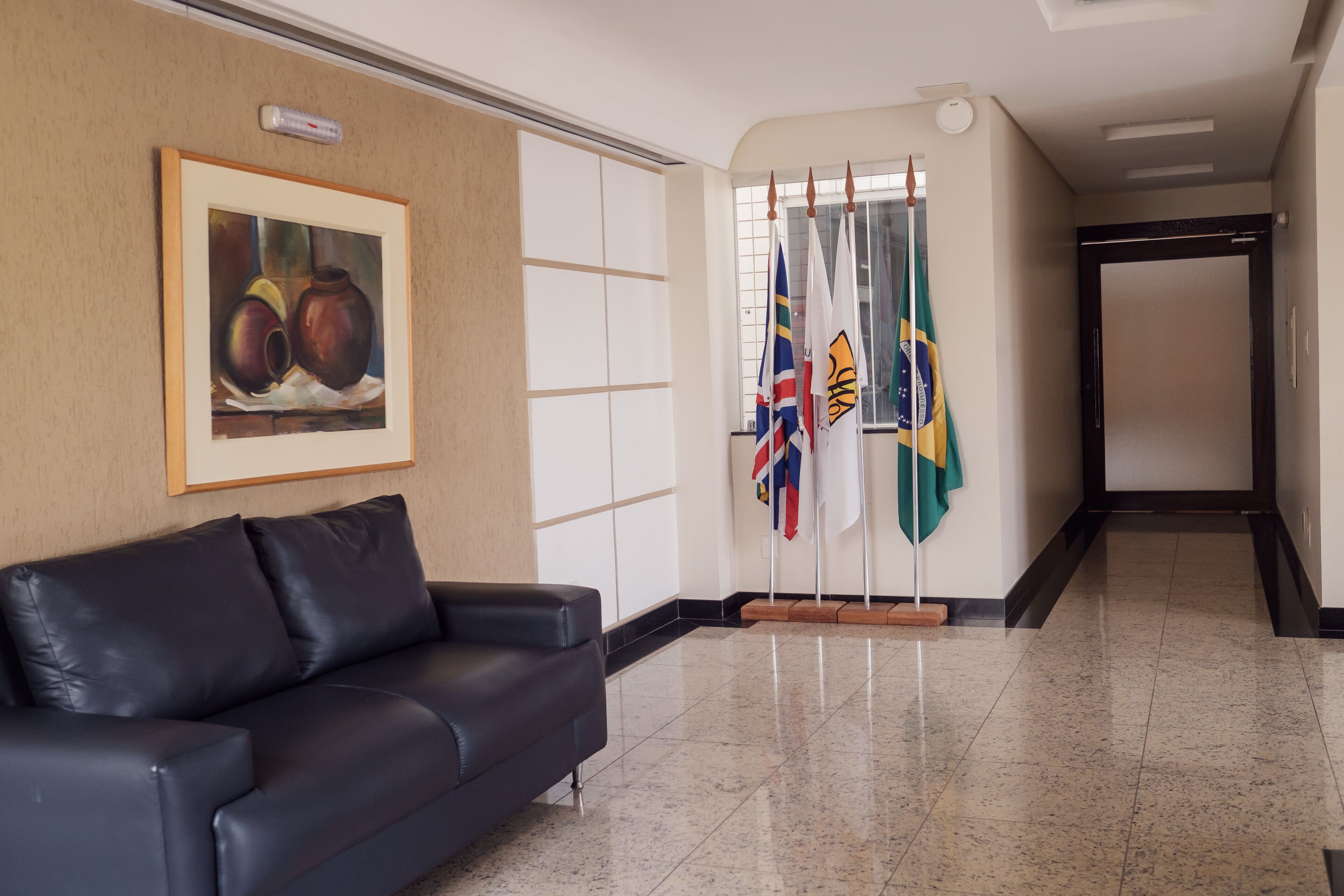 Un hall d’entrée avec un canapé en cuir noir, un tableau encadré et des drapeaux.