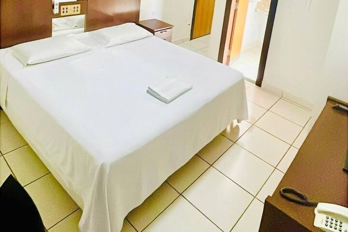 A hotel room with a bed, a desk, a wardrobe, a ceiling fan, and a door leading to another room.