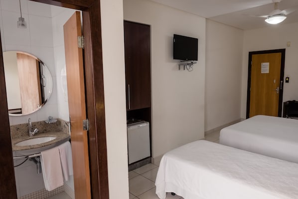 A hotel room with a bed, a TV mounted on the wall, a small refrigerator, and a bathroom with a sink and mirror.