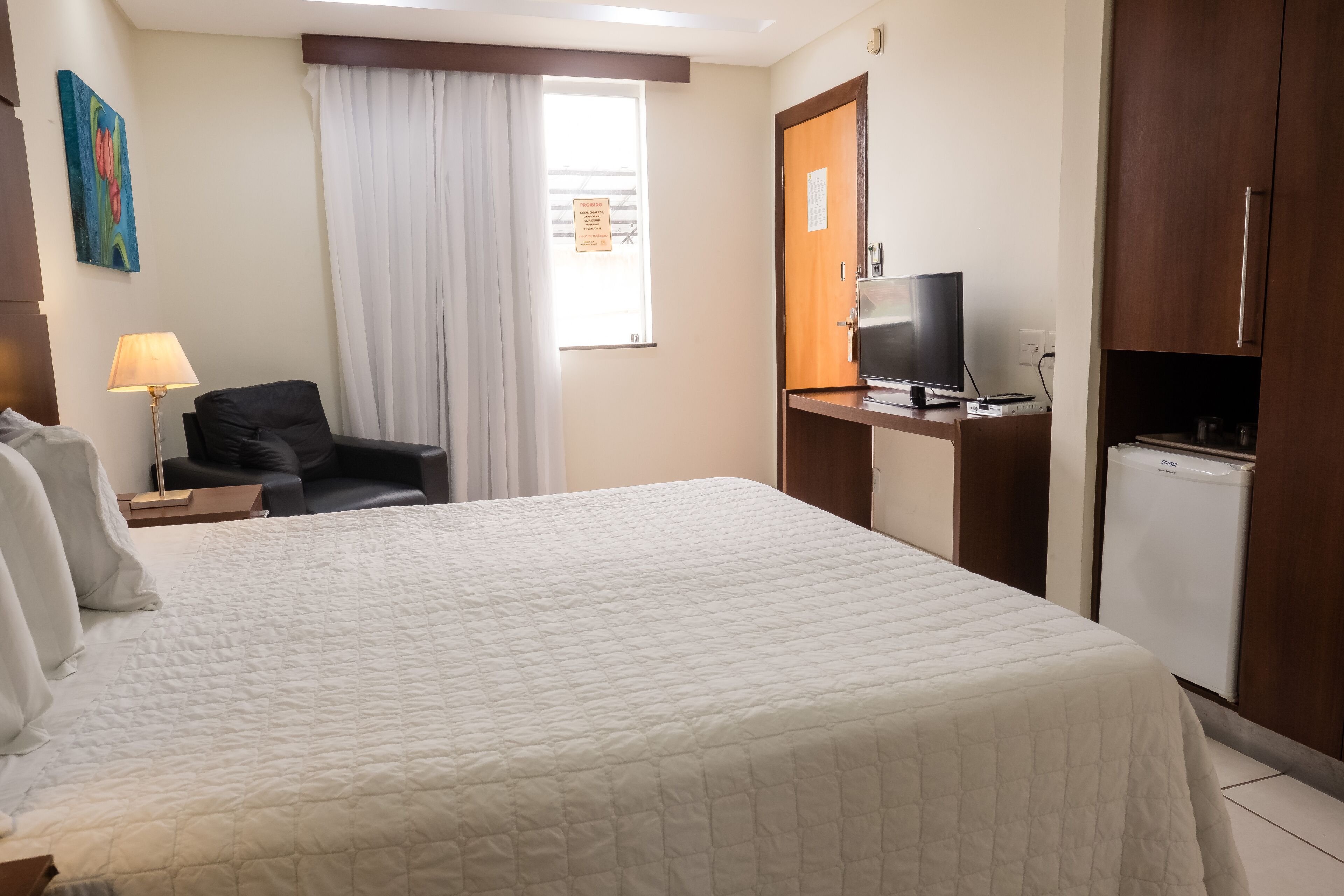 Une chambre d’hôtel équipée d’un lit, d’un bureau avec un ordinateur, d’une télévision et d’un réfrigérateur.