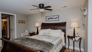 A bedroom with a wooden bed, two bedside tables with lamps, a ceiling fan, and a framed picture on the wall.