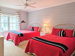 Une chambre avec deux lits, un ventilateur de plafond, une table de chevet avec une lampe et une fenêtre avec des rideaux.