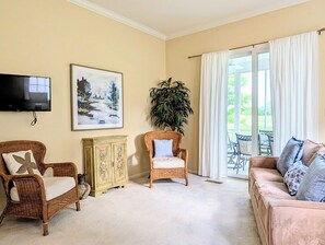 A living room with a flat-screen TV, a painting, a wicker chair, a cabinet, and a sofa.