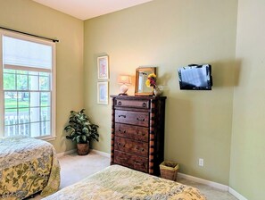 A bedroom with two beds, a dresser, a potted plant, and a wall-mounted TV.