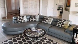 Een moderne woonkamer met een gebogen grijze modulaire bank, een glazen salontafel en decoratieve kussens.