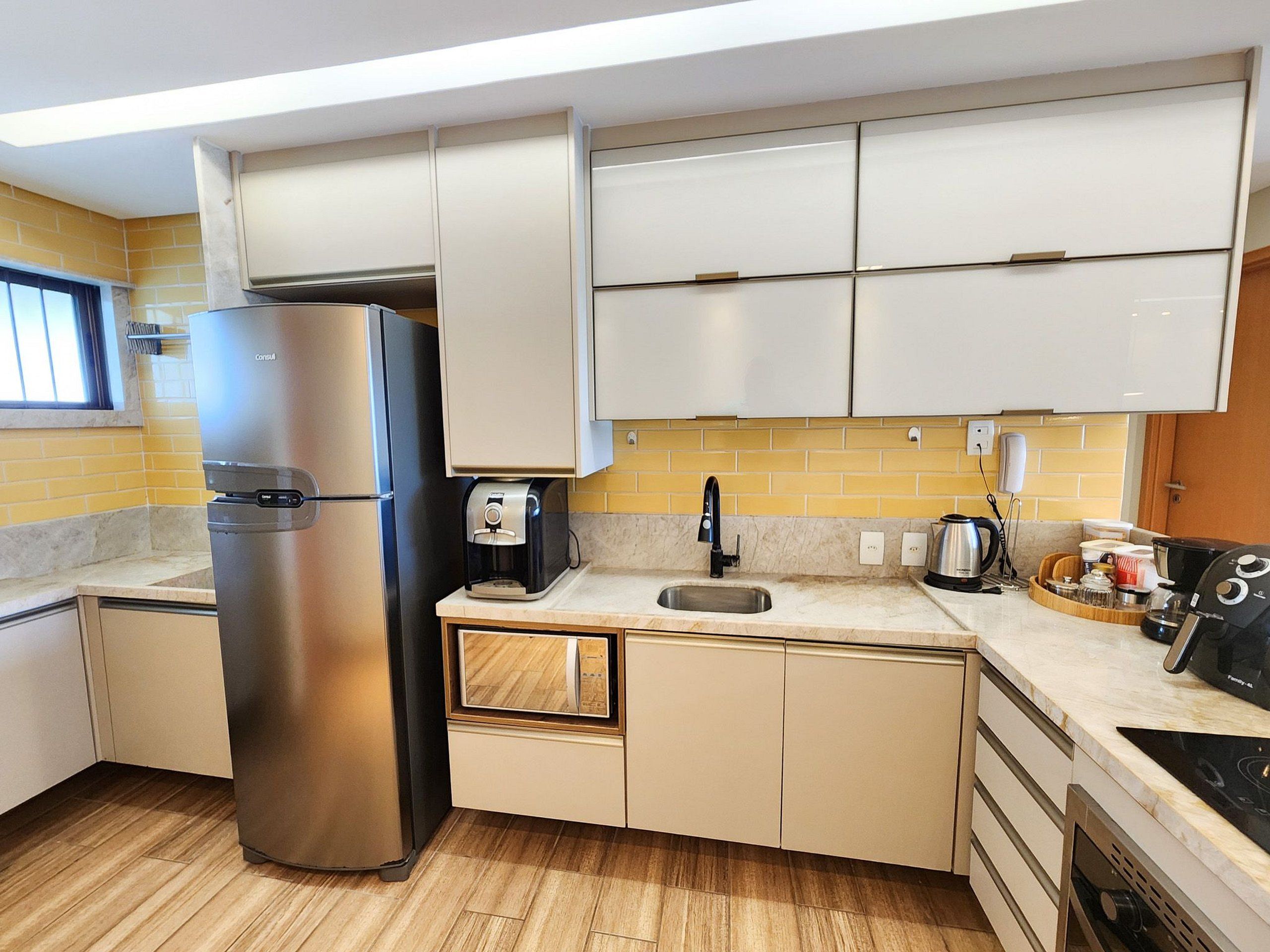 A compact kitchen with a stainless steel refrigerator, a coffee maker, a sink, and a microwave.