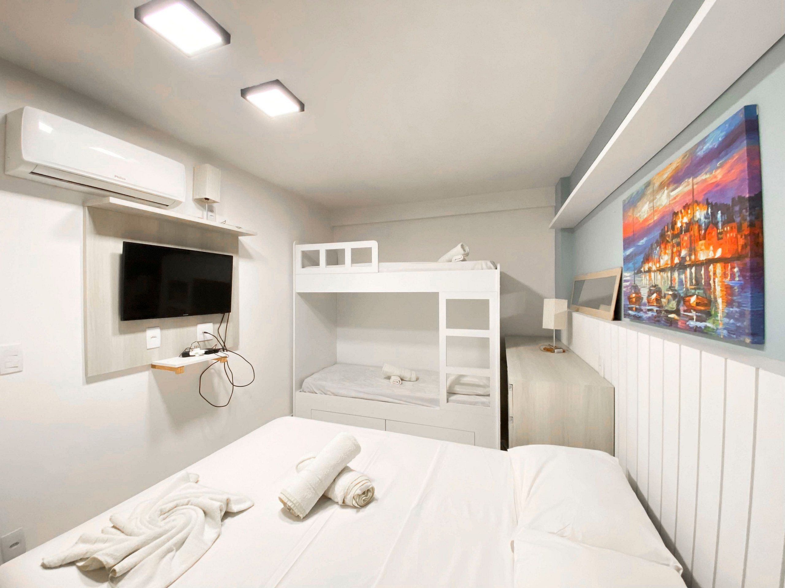 Een hotelkamer met een stapelbed, een flatscreen televisie aan de muur, een schilderij en een nachtkastje met een lamp.